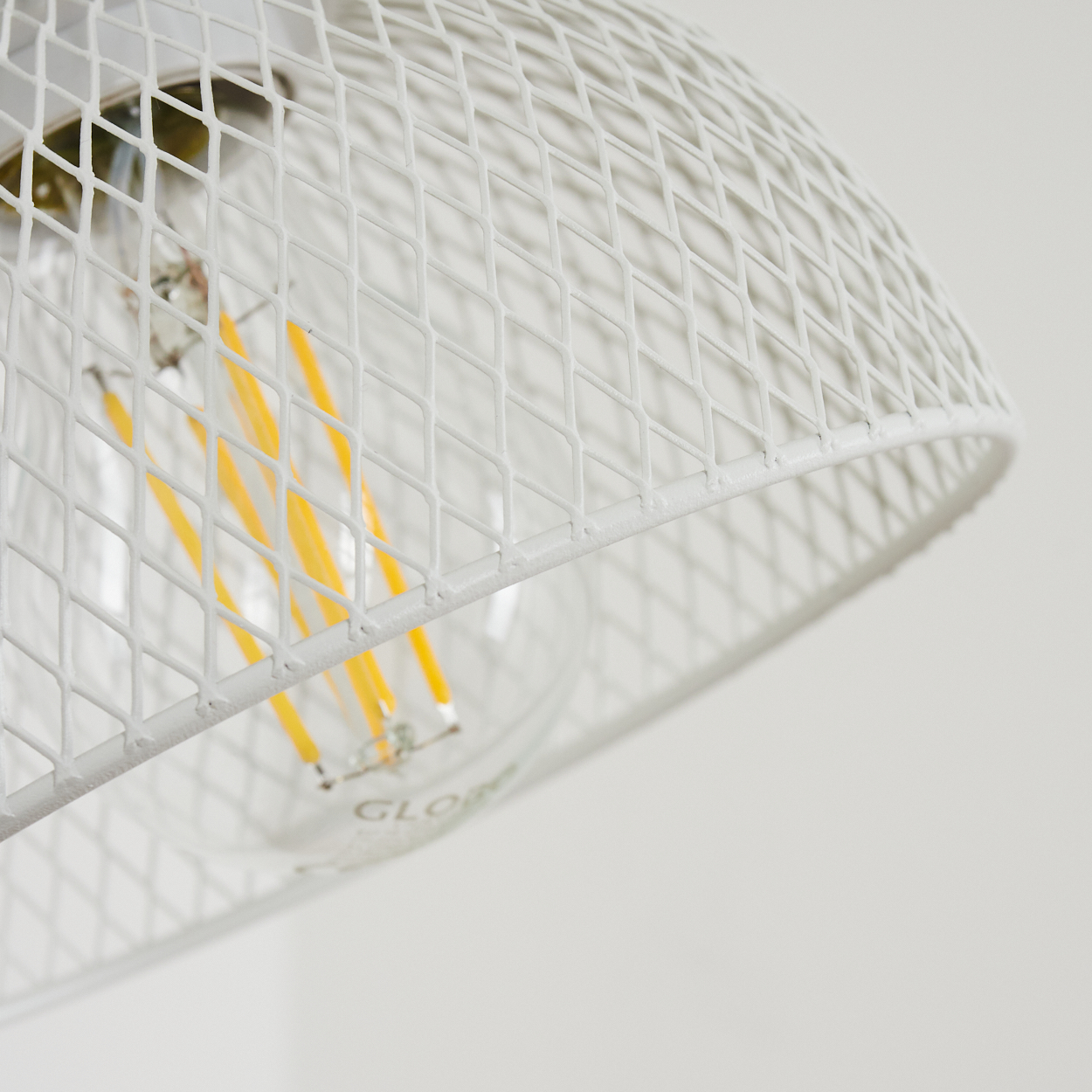 Nahaufnahme einer weißen Lampe mit sichtbarem Leuchtmittel und gelben Glühfäden.