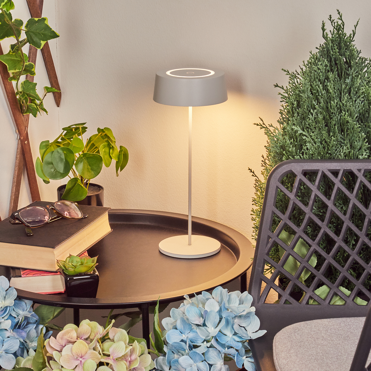 Graue Lampe auf schwarzem Tisch mit Büchern, Pflanzen und Blumen.