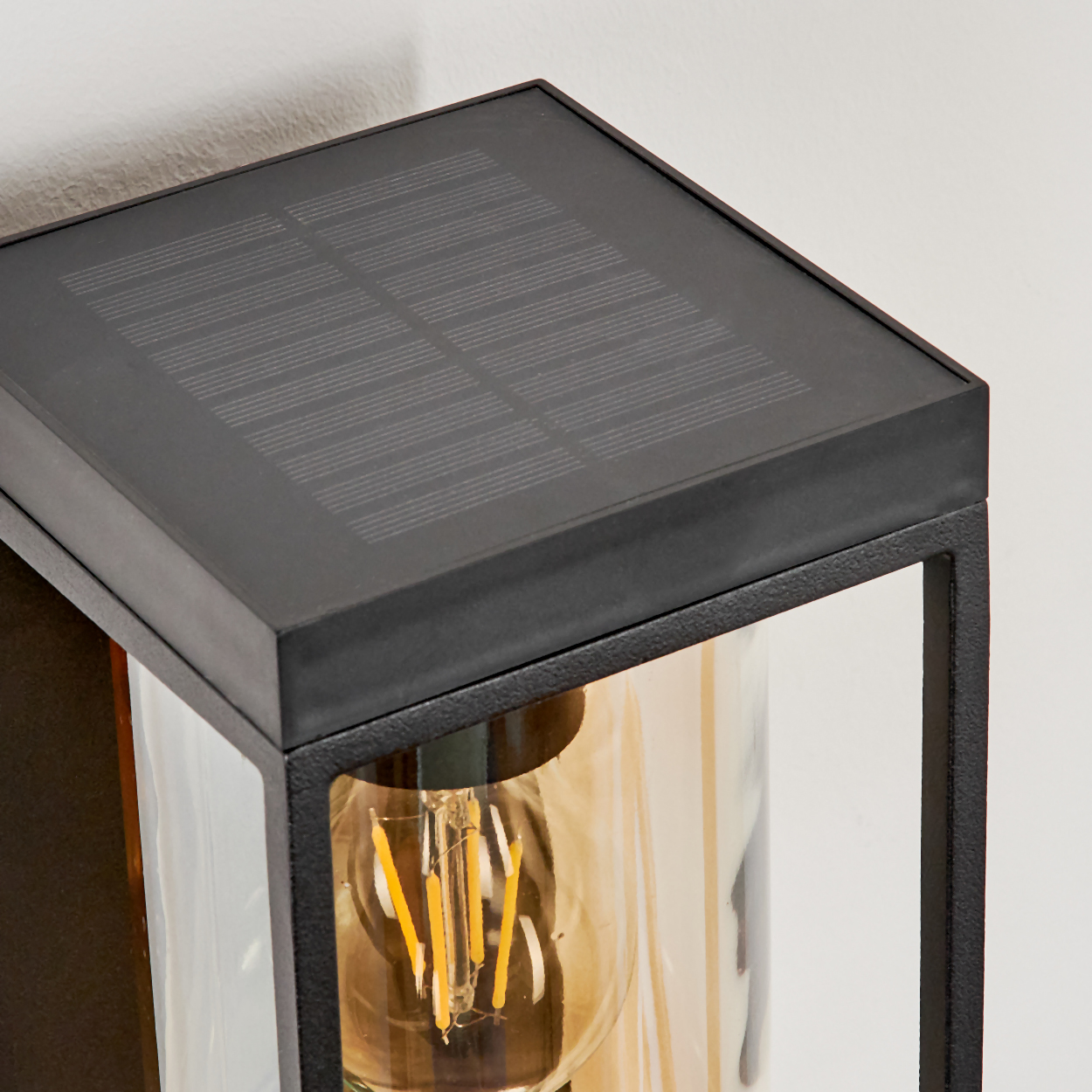 Schwarze Wandleuchte mit Solarpanel und sichtbarer Glühbirne.
