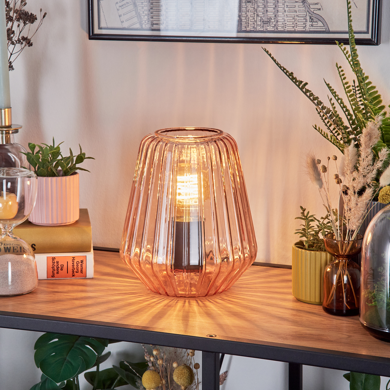 Eine orangefarbene Glaslampe mit Glühbirne steht auf einem Holzregal.