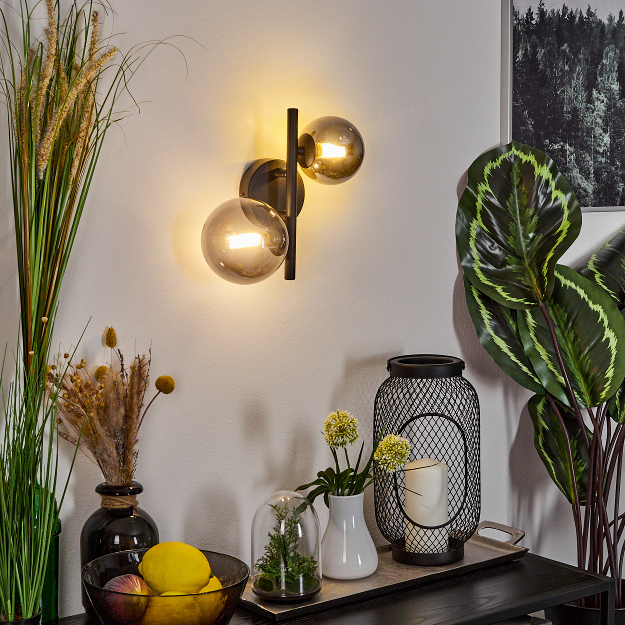 Eine Wandlampe mit zwei rauchfarbenen Glaskugeln beleuchtet eine Wand.