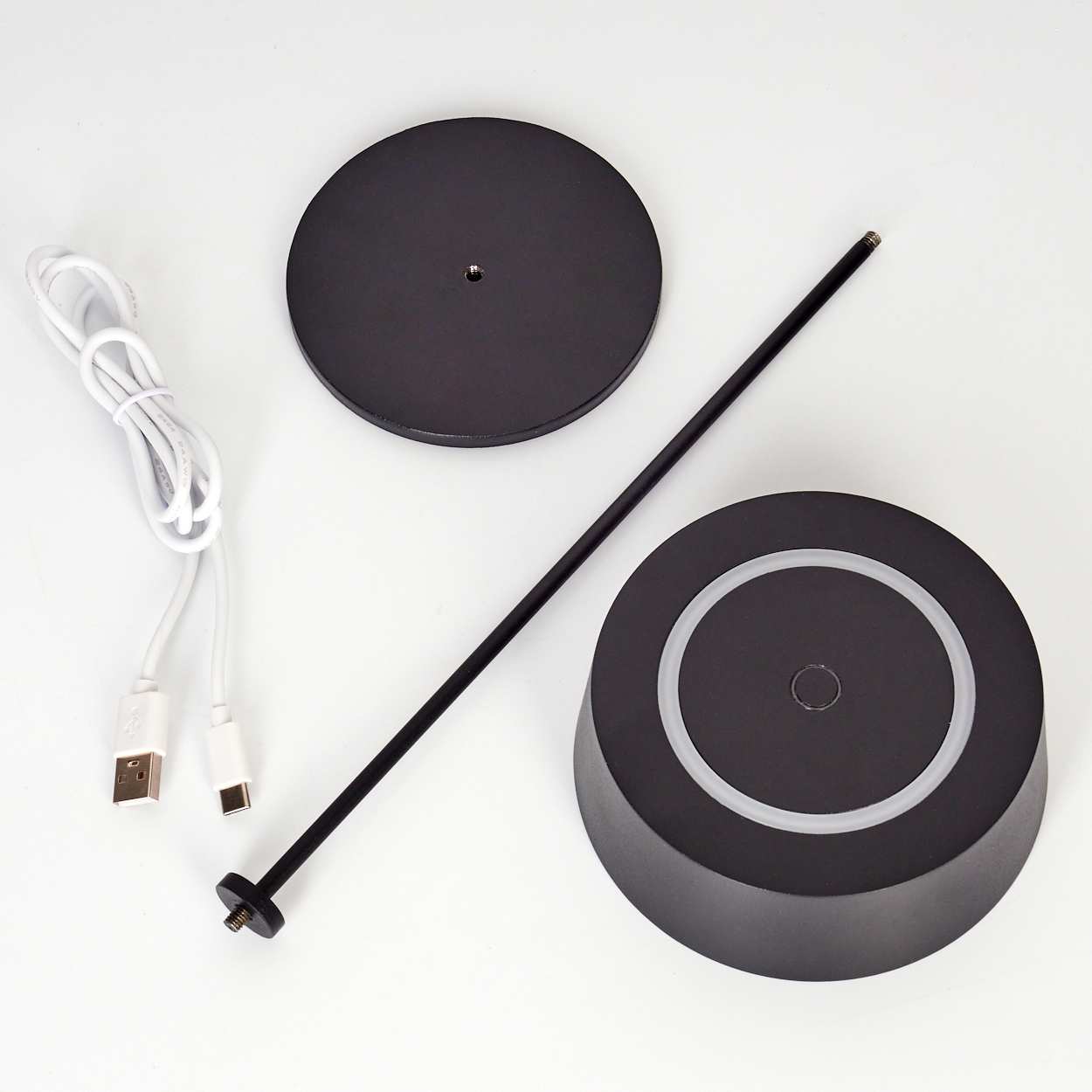 Schwarze Sockelteile, Stab und USB-Kabel auf weißem Hintergrund.