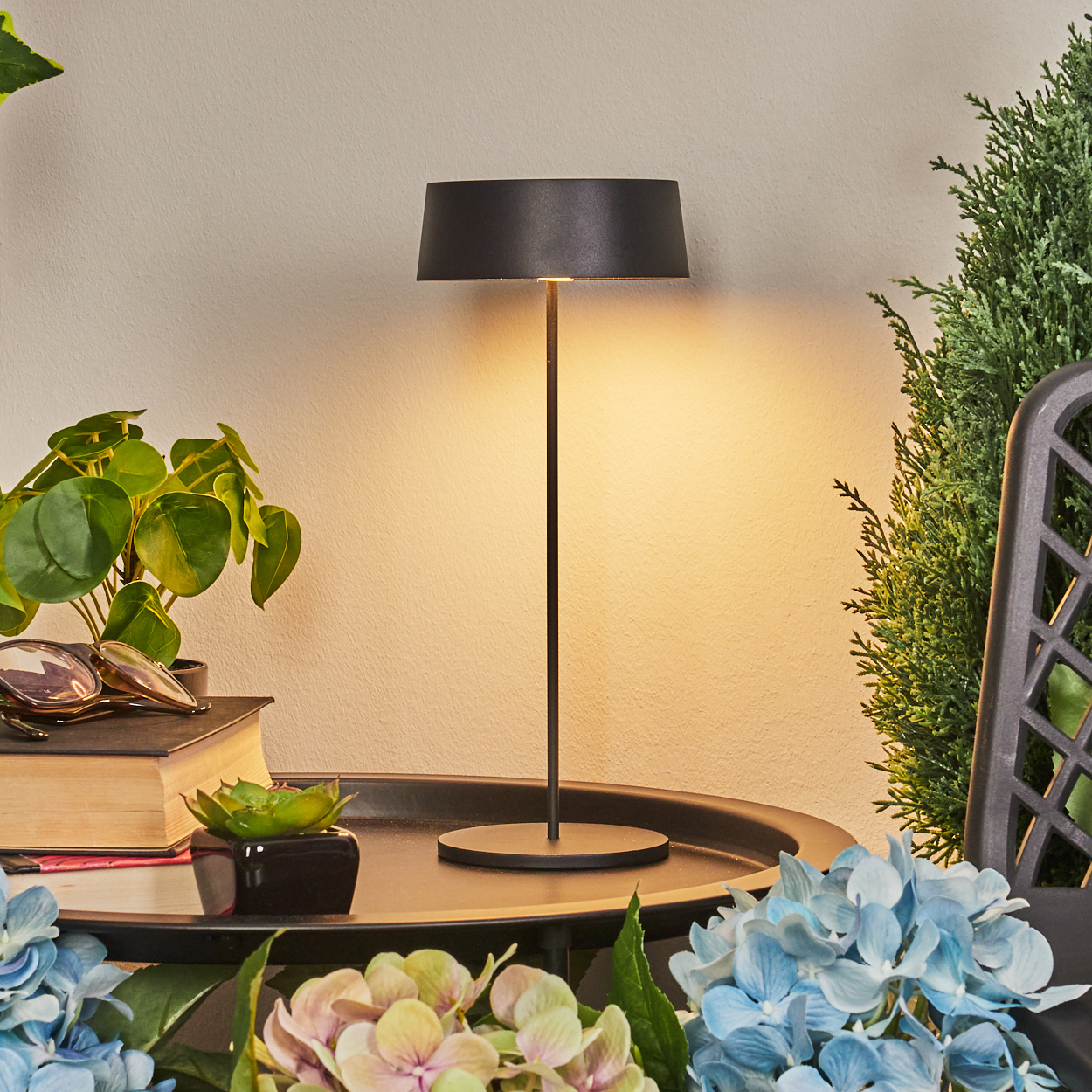 Eine schwarze Tischlampe steht auf einem Tablett mit Pflanzen und Blumen.