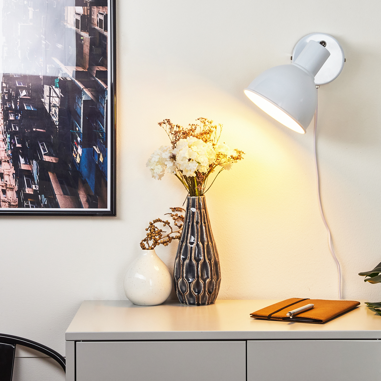 Ein Wandlicht beleuchtet zwei Vasen mit Blumen, ein Notizbuch und ein Bild.