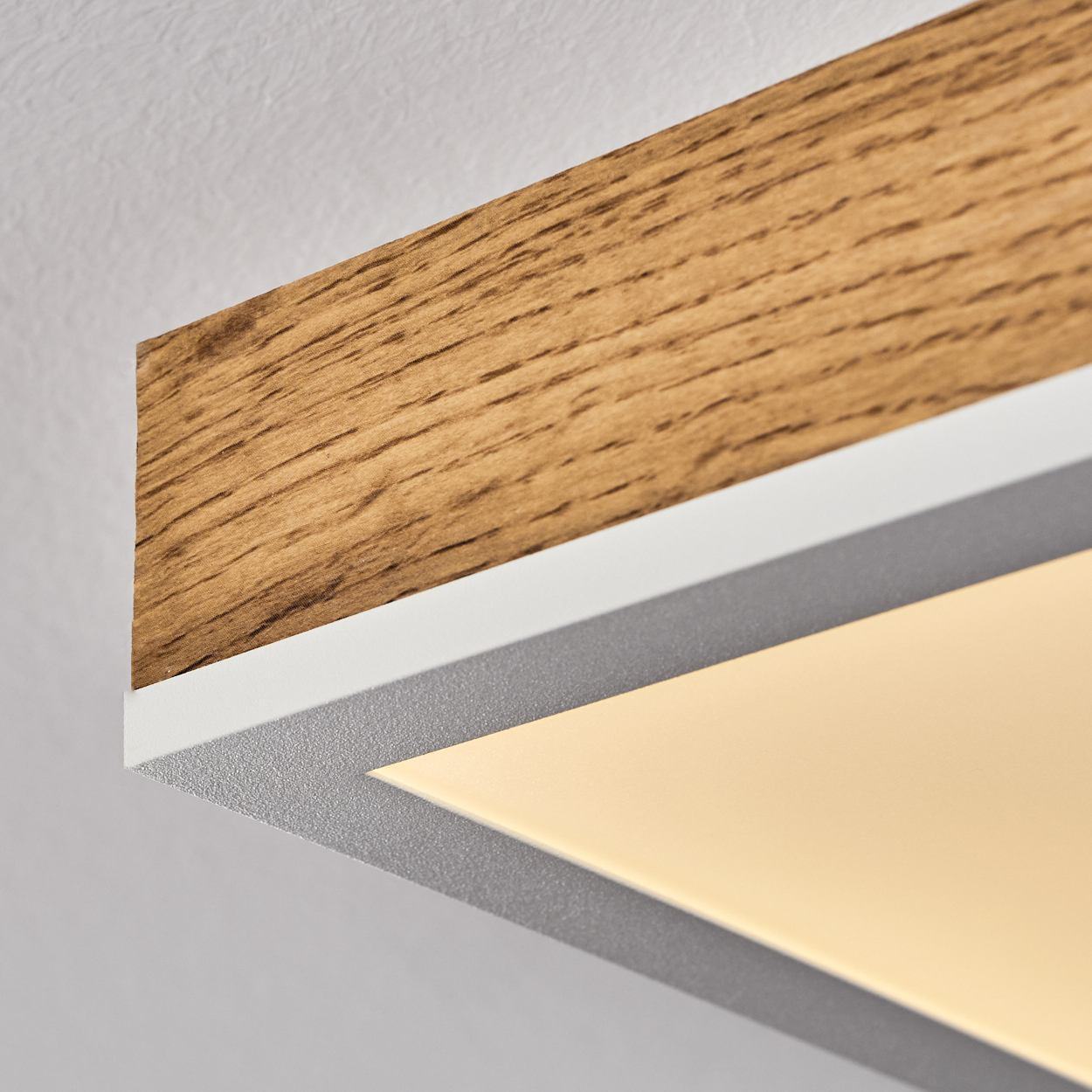 Nahaufnahme einer Deckenleuchte mit Holzmaserung, weißem Rahmen und gelbem Licht.
