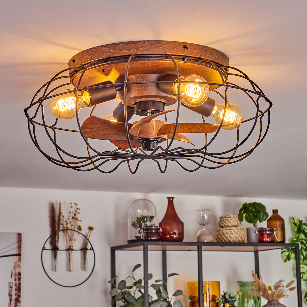 Deckenventilator mit Holzoberfläche, schwarzem Drahtkäfig und Glühbirnen.
