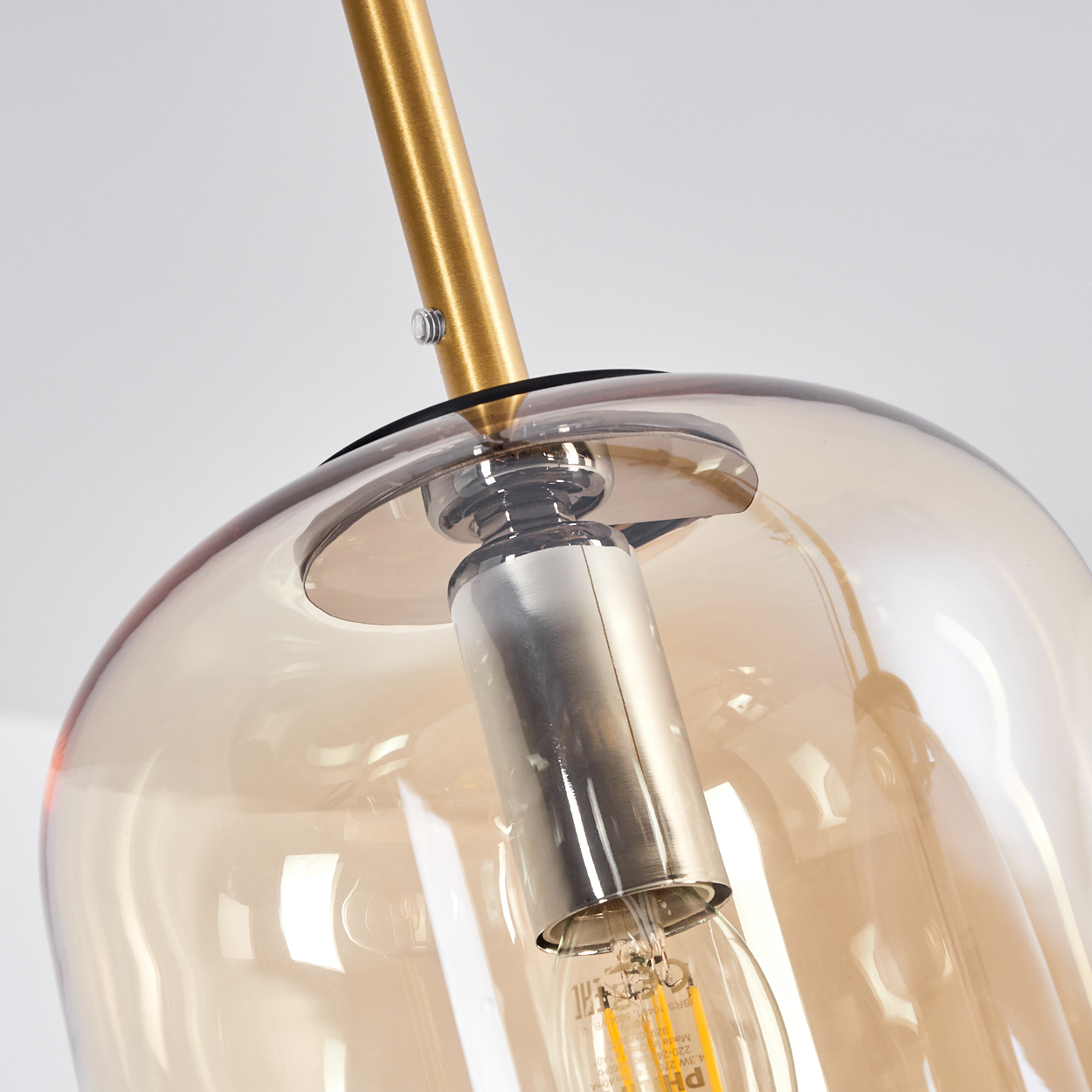 Nahaufnahme einer goldfarbenen Lampe mit bernsteinfarbenem Glasschirm und Glühbirne.