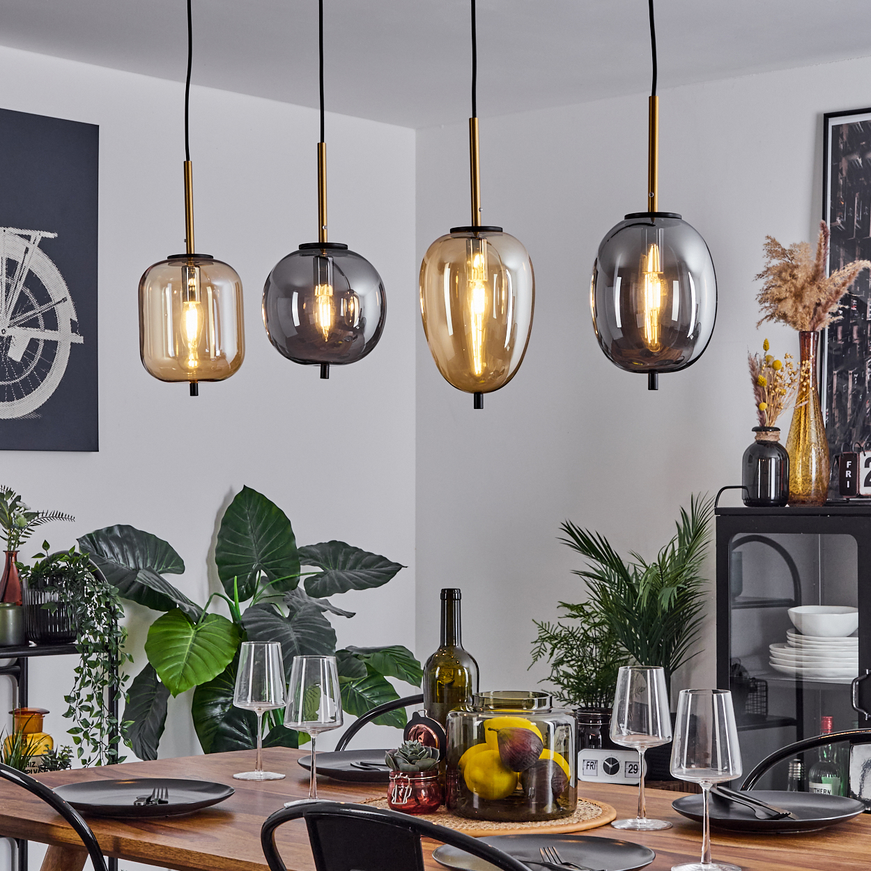 Vier Hängeleuchten über einem Holztisch mit Tellern, Gläsern und Obst.