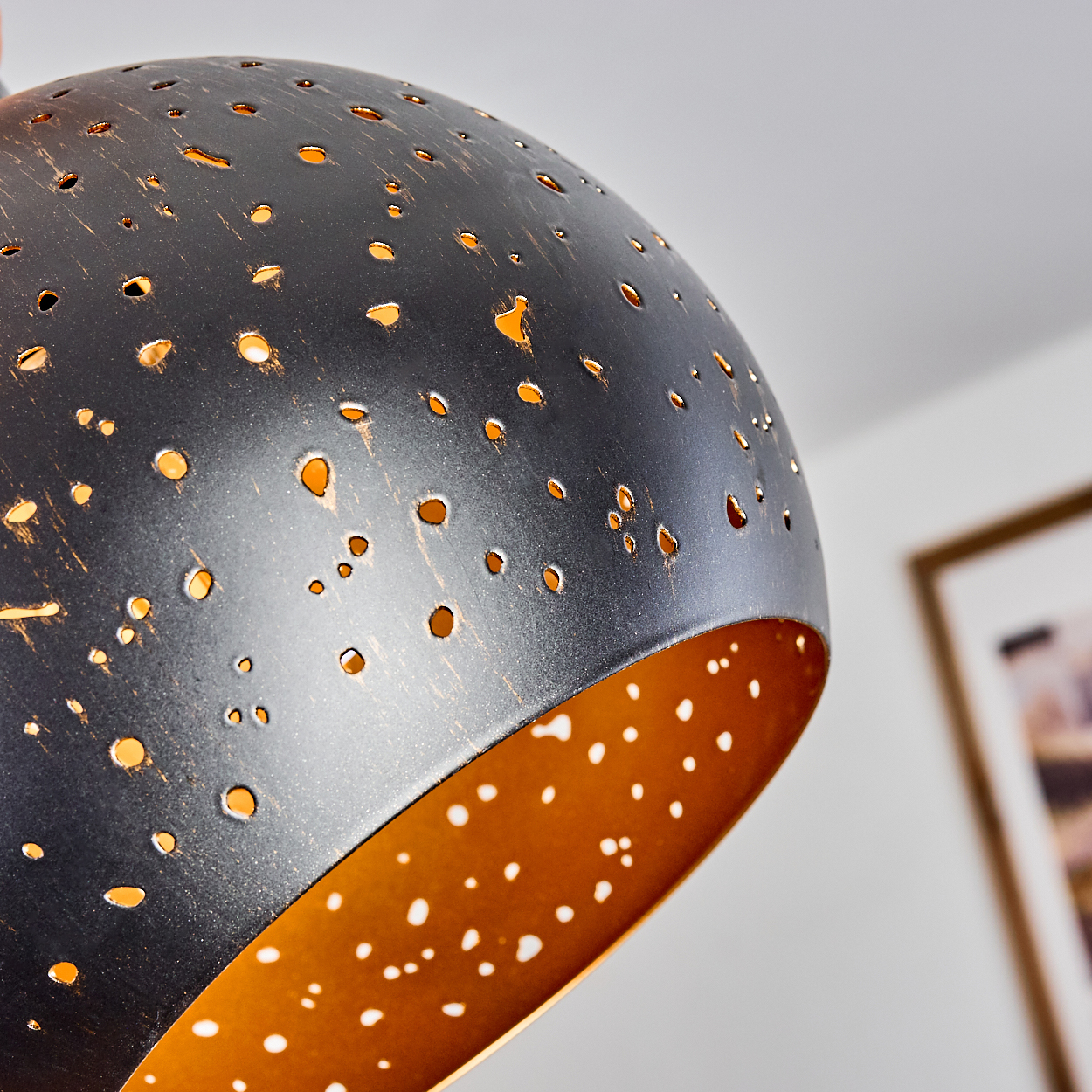 Eine dunkle Lampe mit vielen kleinen Löchern, die goldenes Licht durchscheinen lassen.