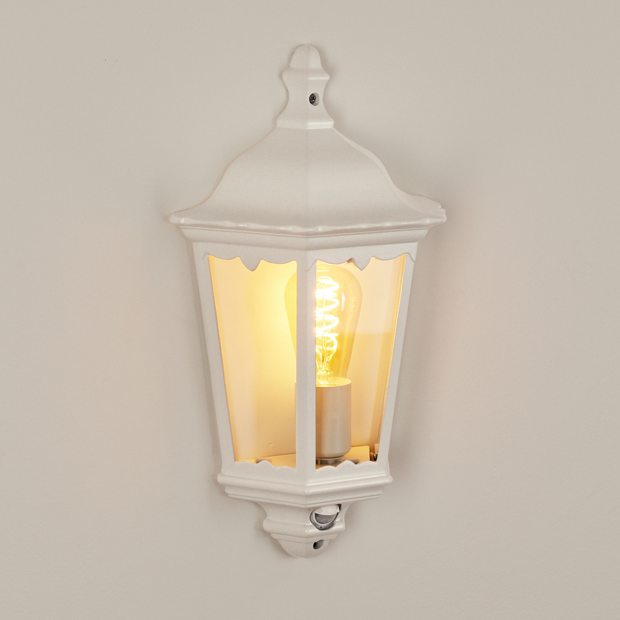 Eine weiße Wandlaterne mit Glühbirne leuchtet vor einer cremefarbenen Wand.