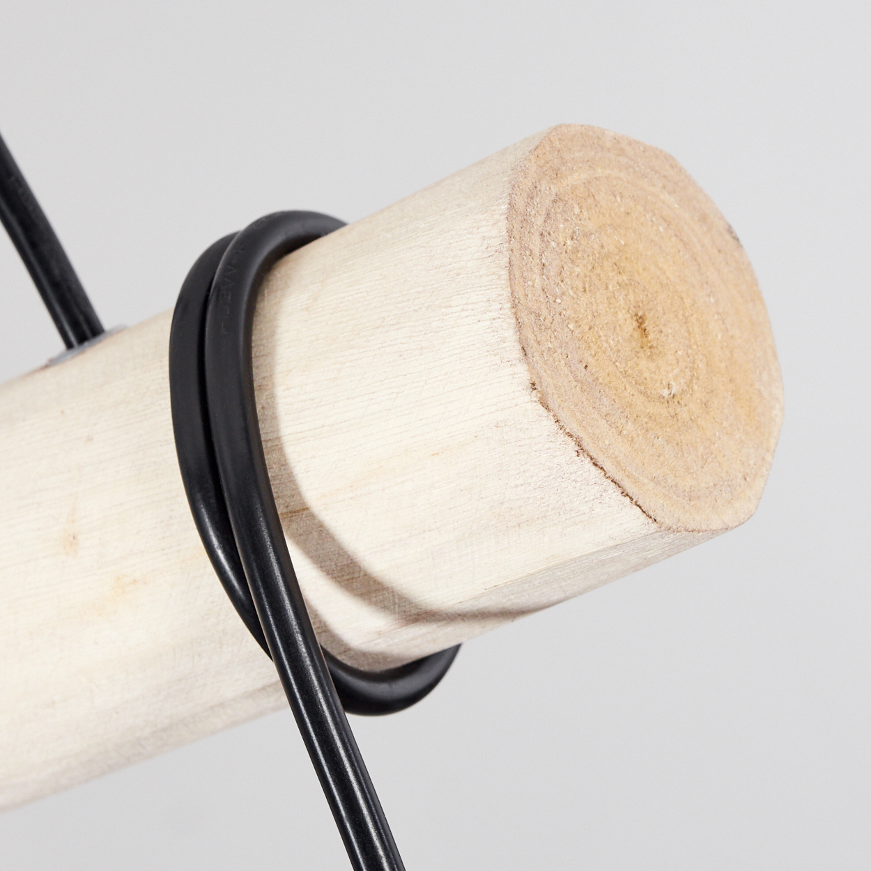 Ein schwarzes Kabel wickelt sich um ein helles Holzstück auf grauem Hintergrund.