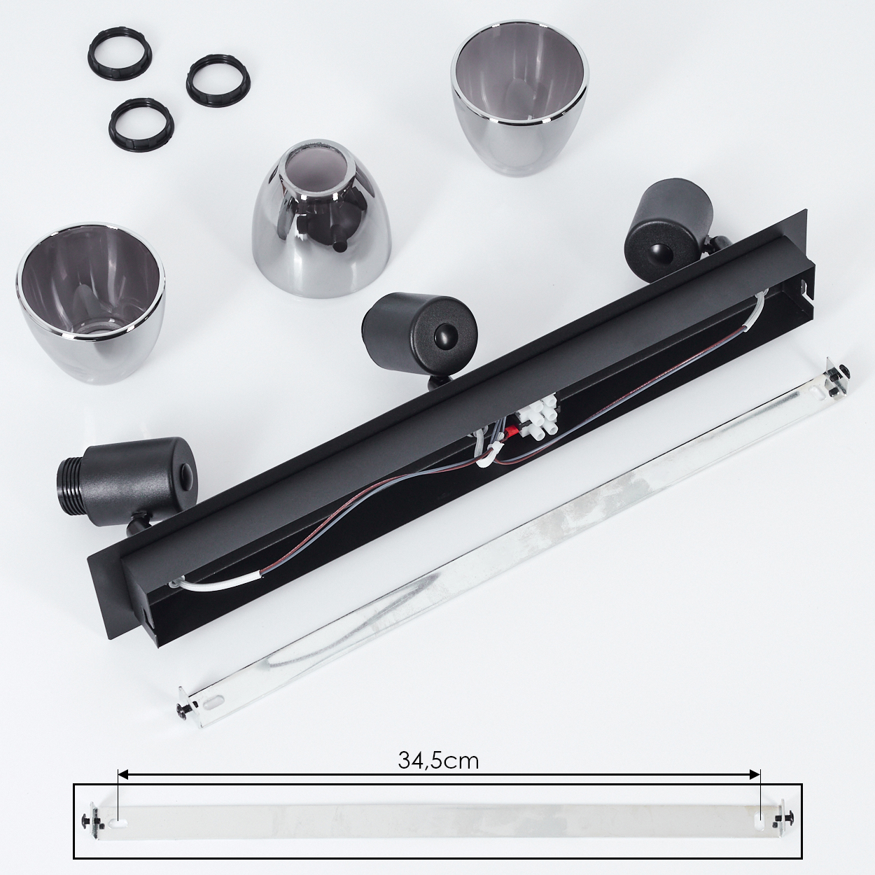 Teile einer schwarzen Lampe, darunter Lampenschirme, Fassungen und ein langer Metallstreifen.