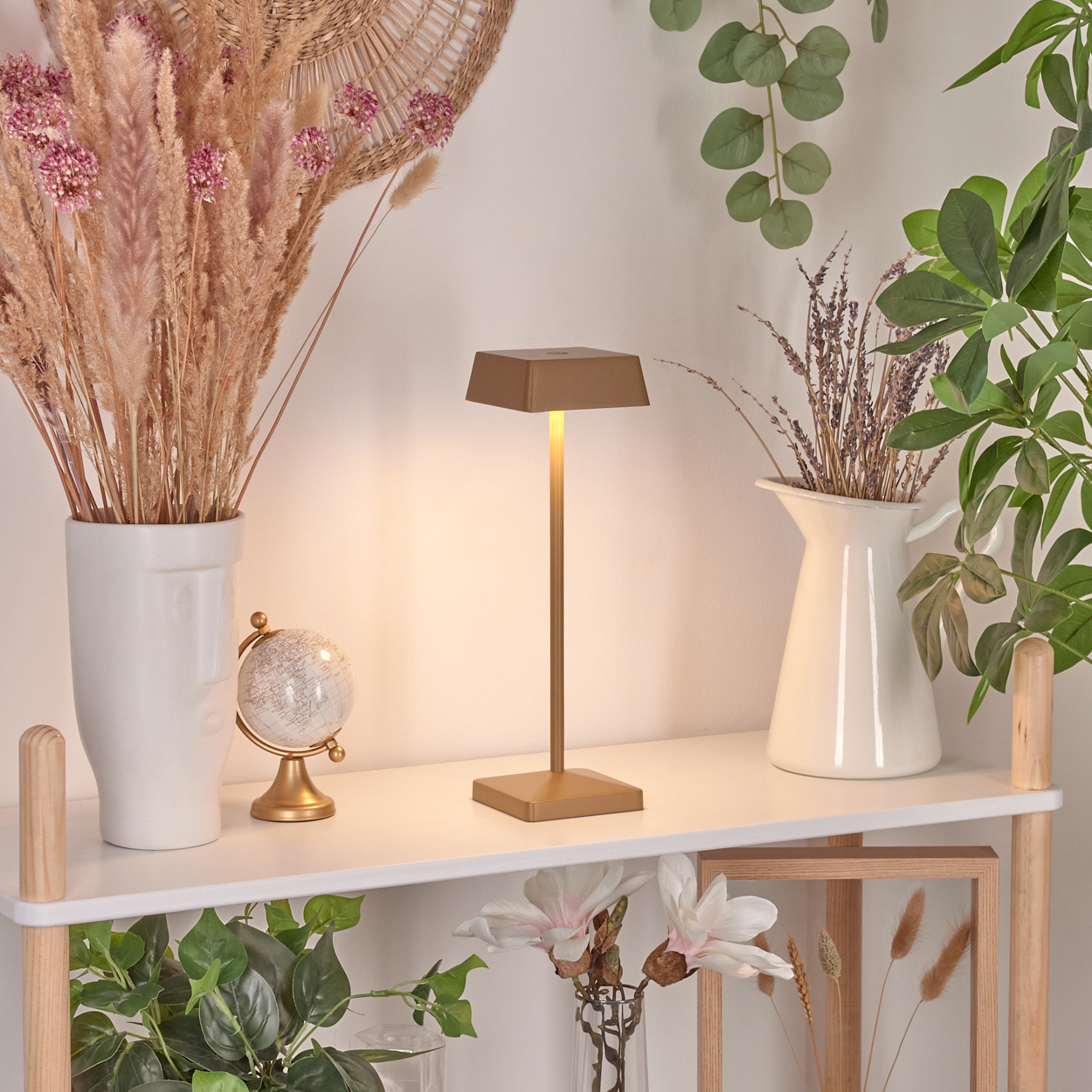 Eine goldene Lampe leuchtet auf einem Regal mit Trockenblumen und einer Vase.