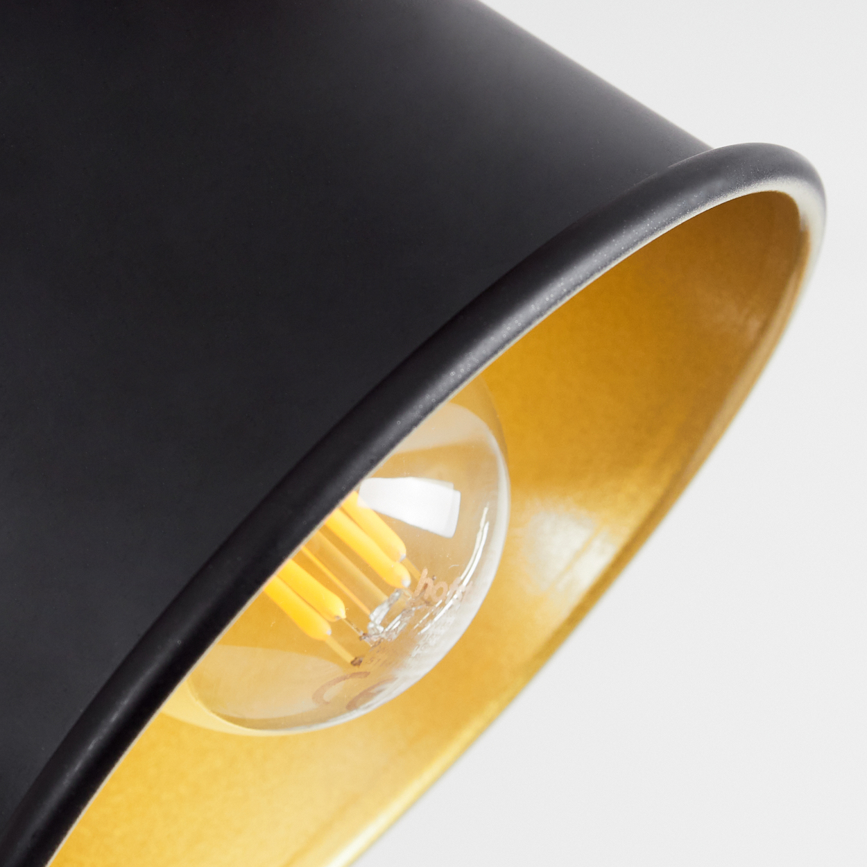 Nahaufnahme einer schwarzen Pendelleuchte mit goldener Innenseite und sichtbarer Glühbirne.