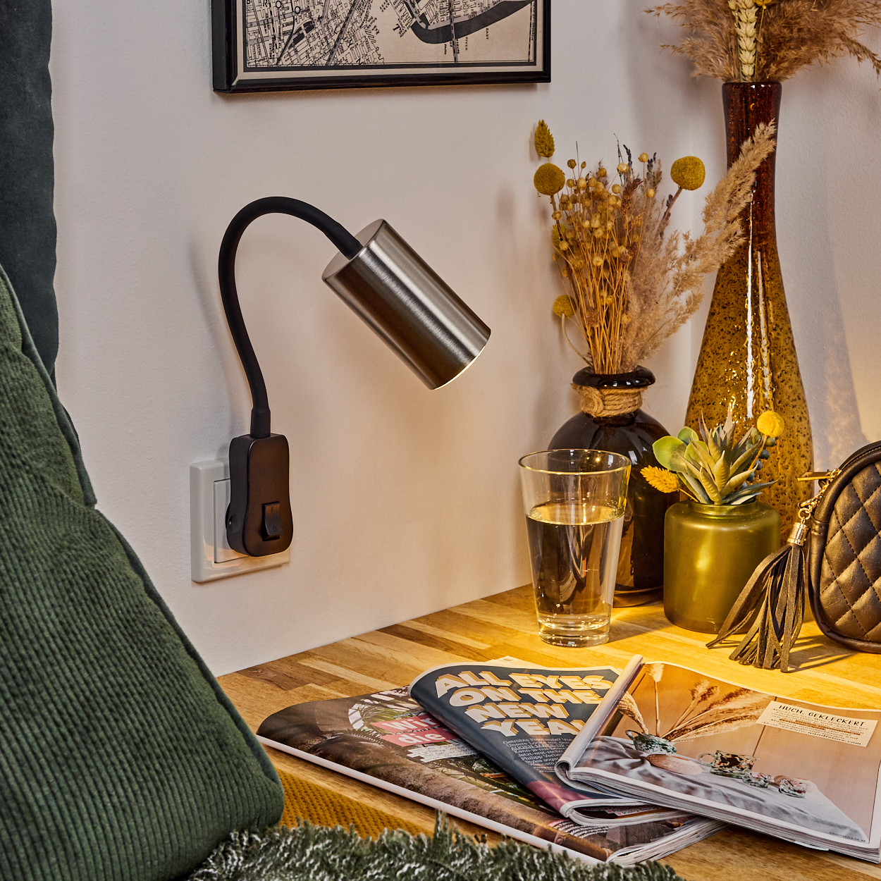 Ein Schreibtisch mit Lampe, Glas Wasser, Zeitschriften, Vasen und Tasche.