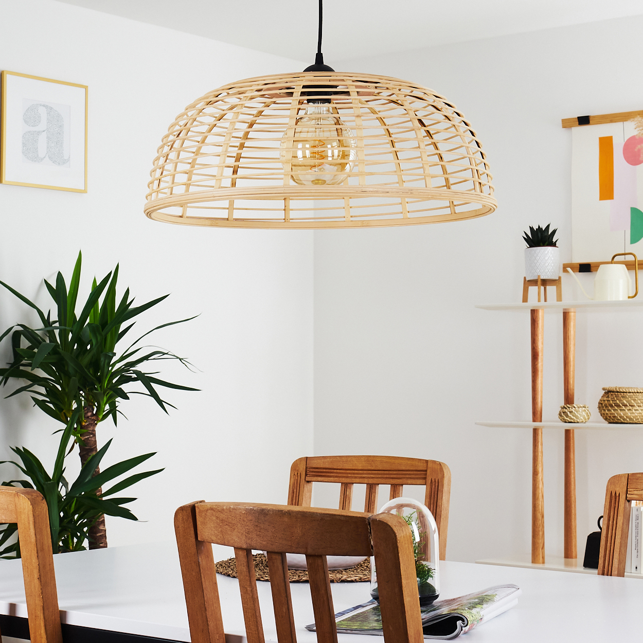 Ein Esszimmer mit einem Esstisch aus weißem Holz, Holzstühlen und einem Rattankorb-Pendelleuchter.