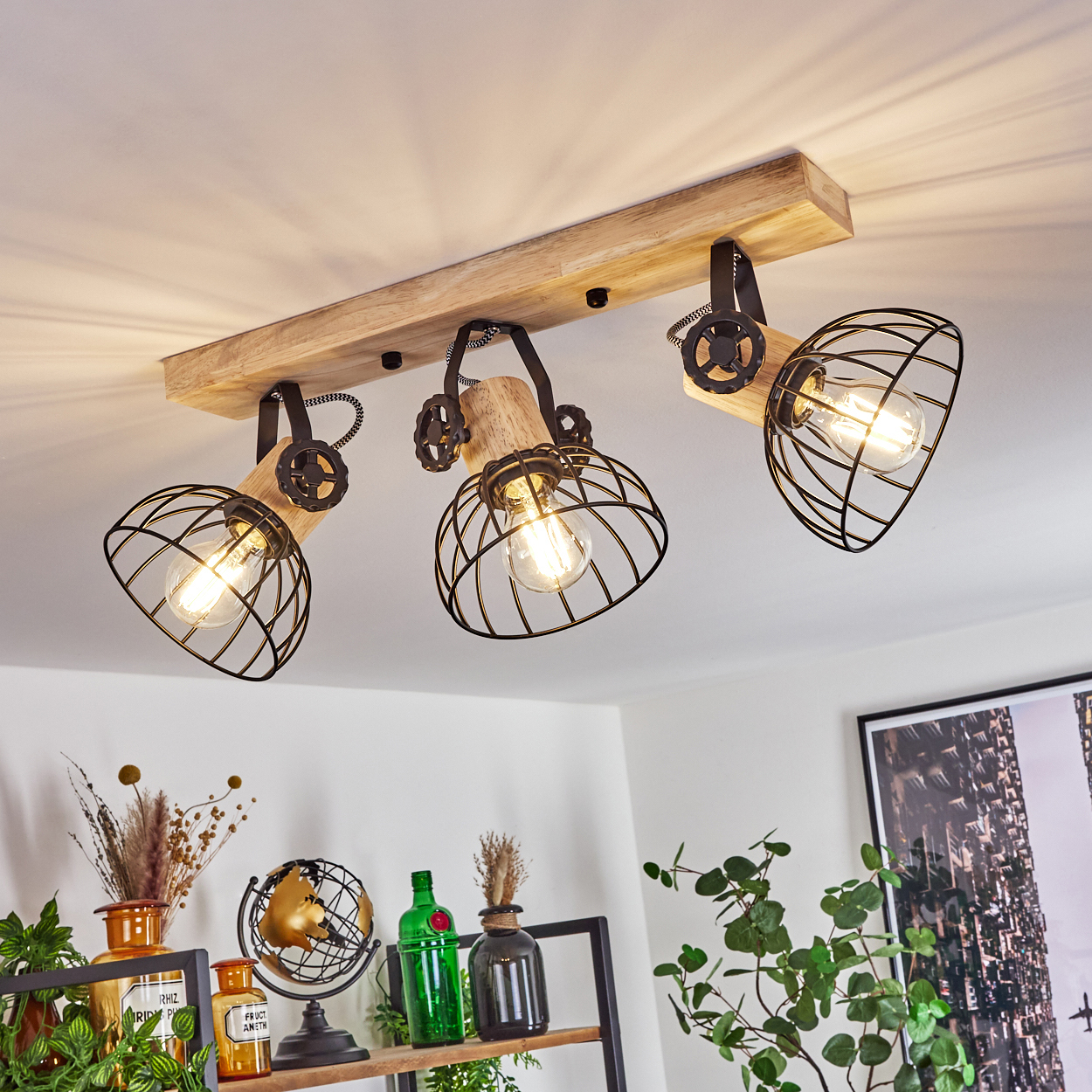 Holzbalken mit drei schwarzen Käfig-Pendelleuchten mit sichtbaren Glühbirnen.