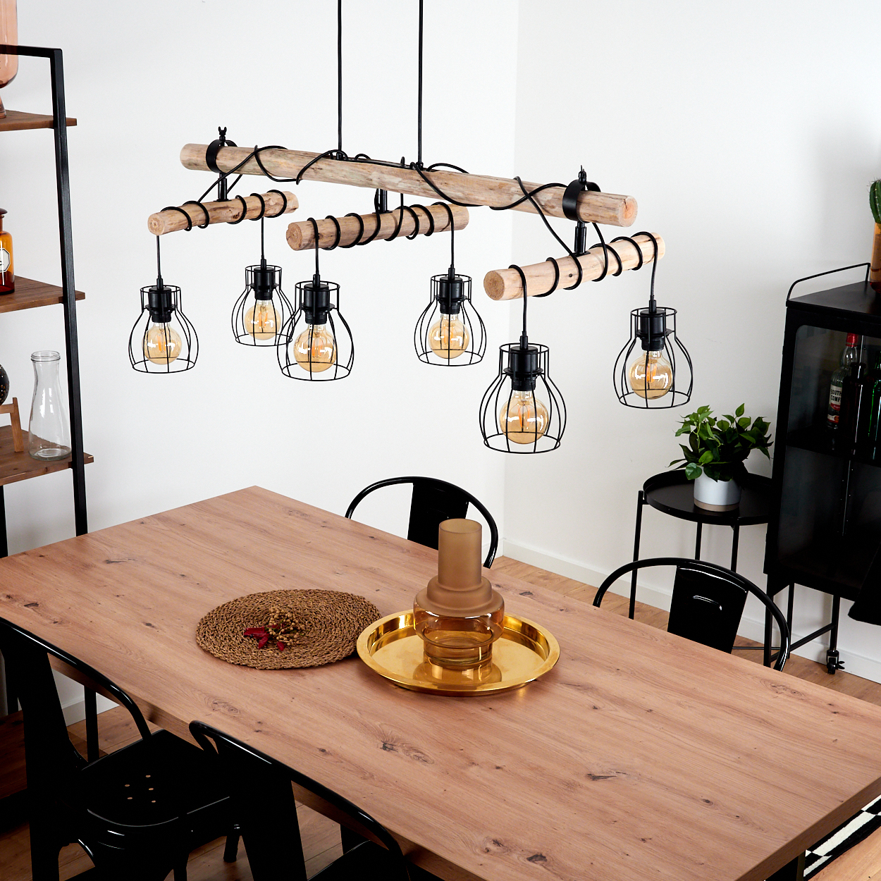 Holz-Kronleuchter mit Glühbirnen über einem Holztisch mit schwarzen Stühlen.