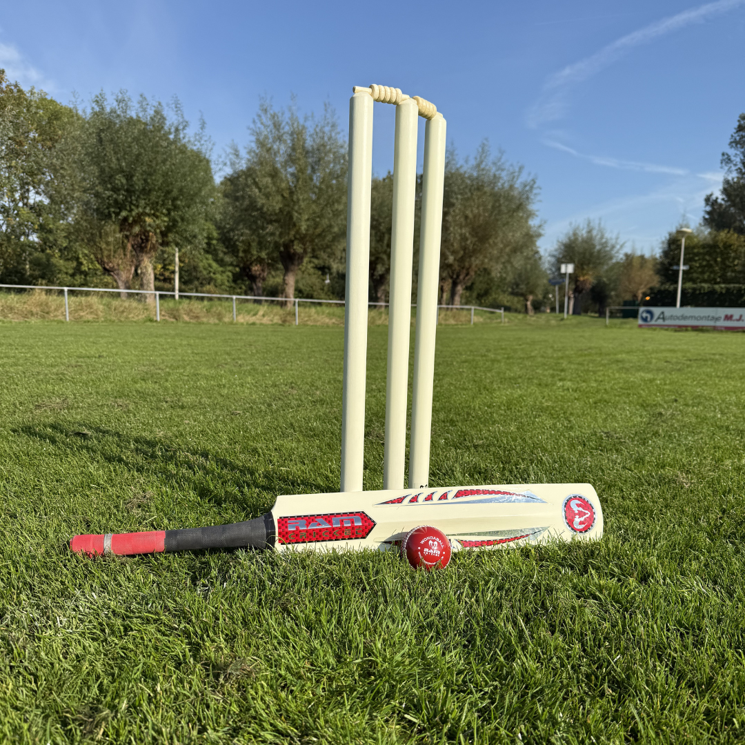Ein Cricket-Schläger und Ball liegen auf dem Rasen vor einem Wicket.