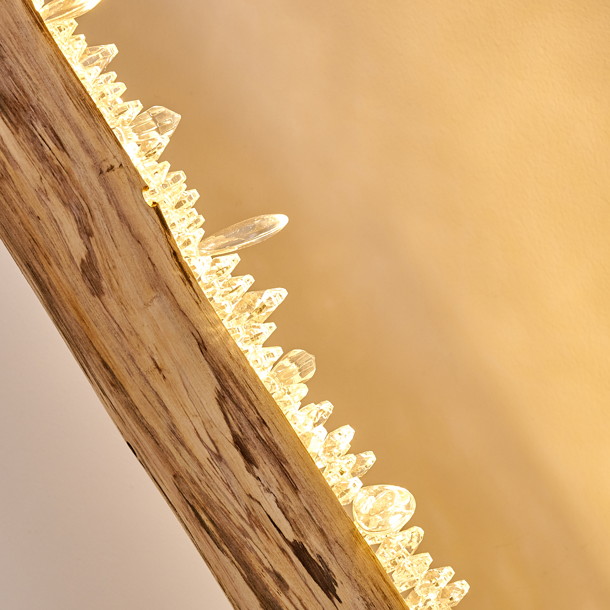Holzbalken mit daran befestigten kristallklaren Schmuckelementen, die Licht reflektieren.