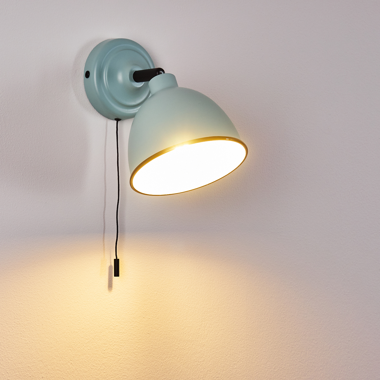 Eine hellblaue Wandleuchte mit goldfarbenem Rand beleuchtet die Wand.