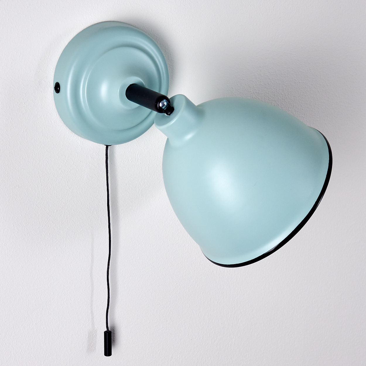 Eine hellblaue Wandleuchte mit schwarzem Zugschalter hängt an einer weißen Wand.