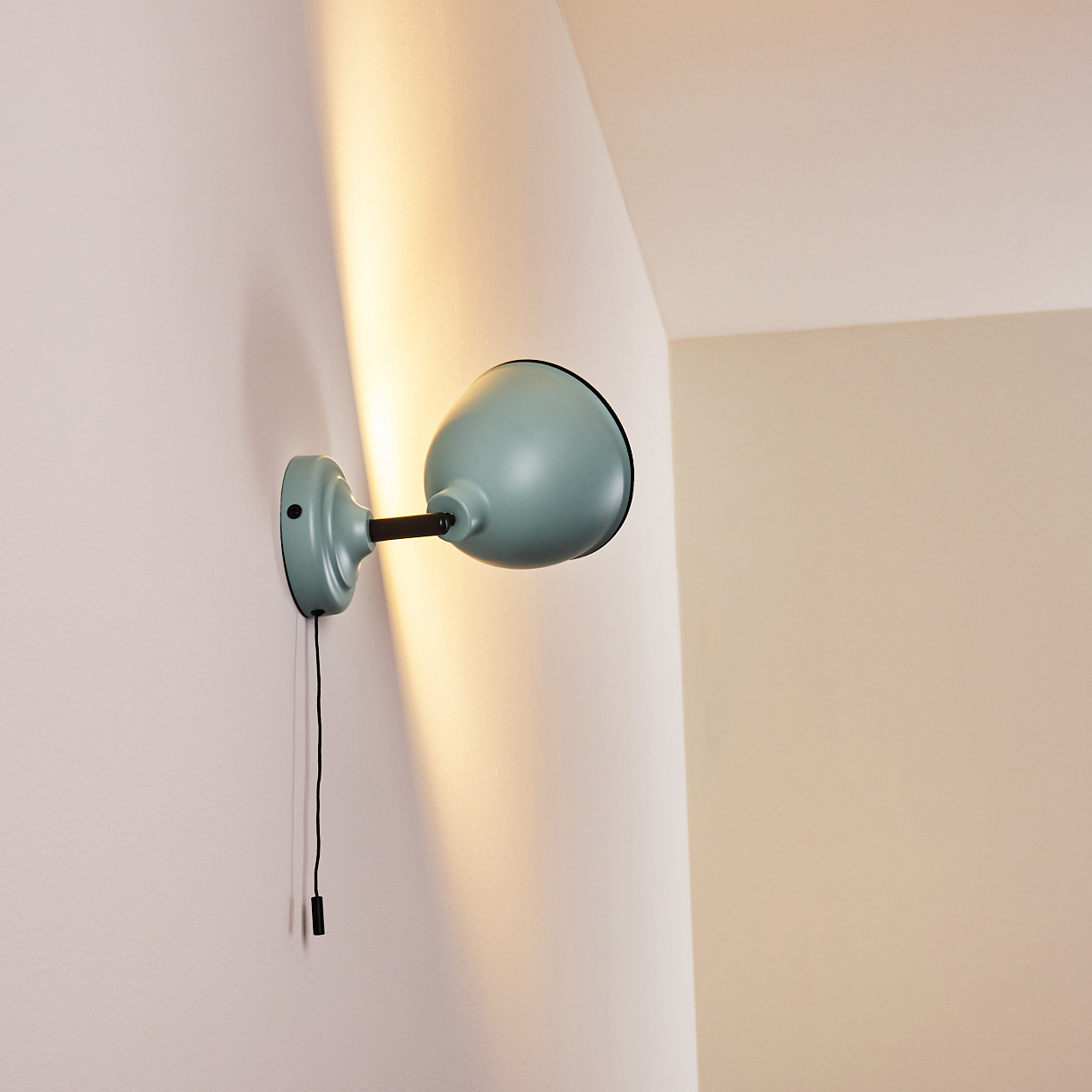 Eine blassgrüne Wandleuchte mit schwarzem Schalter und Kabel an einer weißen Wand.