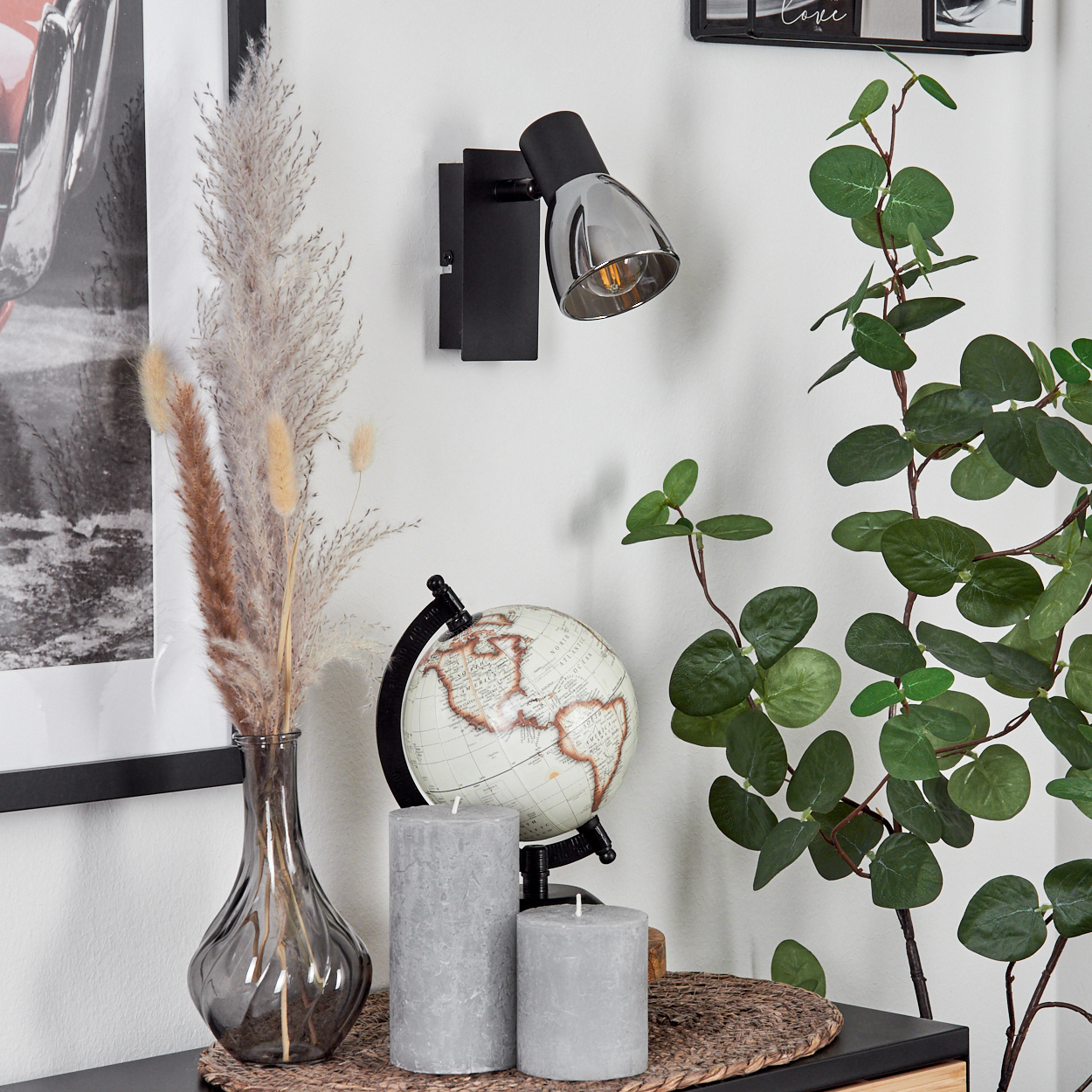 Schwarzer Wandspot über Globus, Vase mit Gräsern und Kerzen.