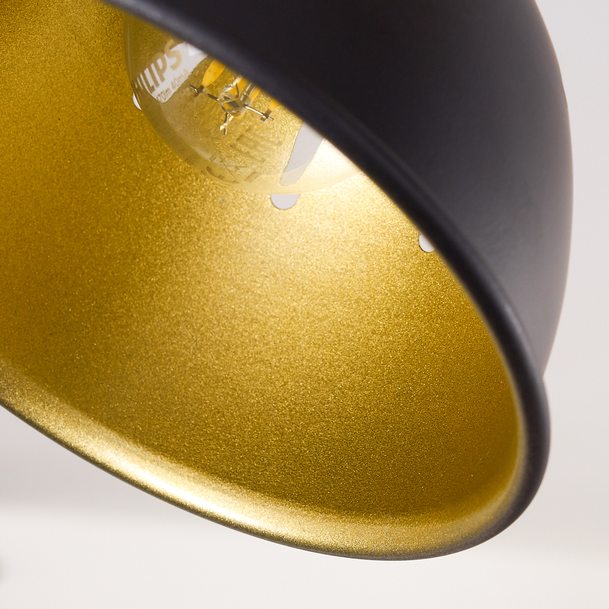 Nahaufnahme einer schwarzen Lampe mit goldenem Inneren und sichtbarer Glühbirne.