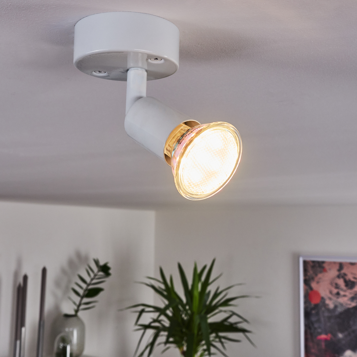 Ein weißer Deckenstrahler mit leuchtender Glühbirne auf weißer Decke.