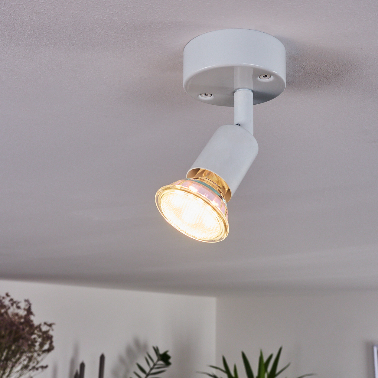 Ein weißer Deckenstrahler mit einer hellen Lampe ist an einer grauen Decke montiert.