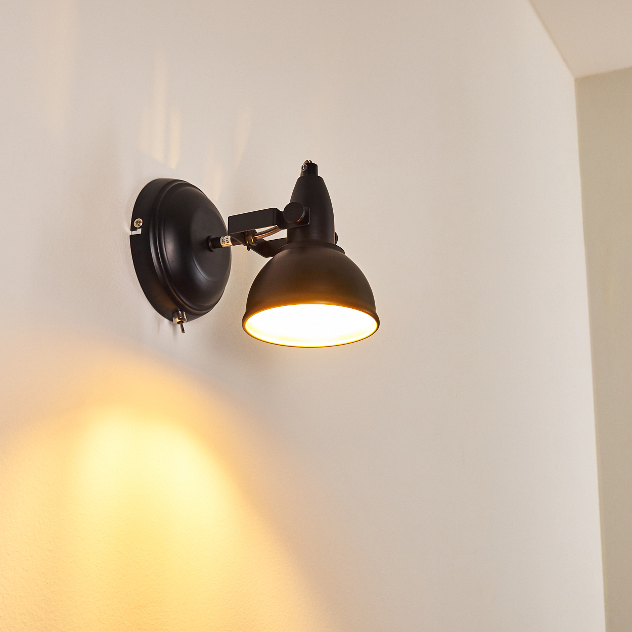 Eine schwarze Wandleuchte mit verstellbarem Arm und Lampenschirm leuchtet.