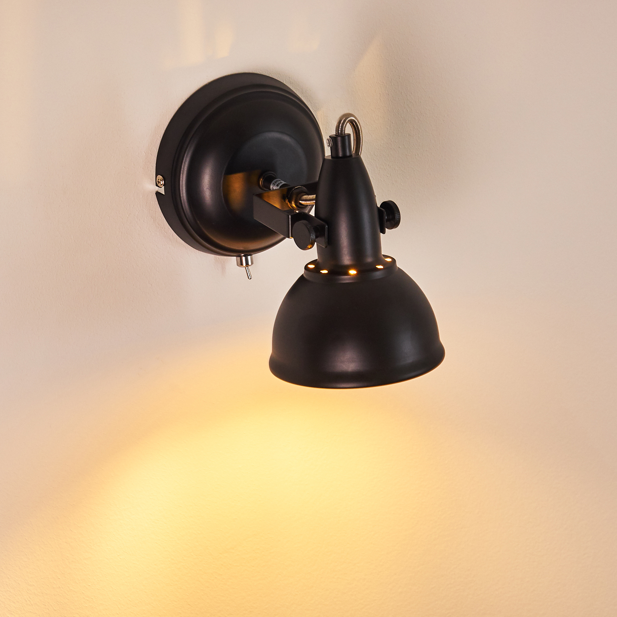 Schwarze Wandlampe mit verstellbarem Arm und Lampenschirm, beleuchtet eine Wand.