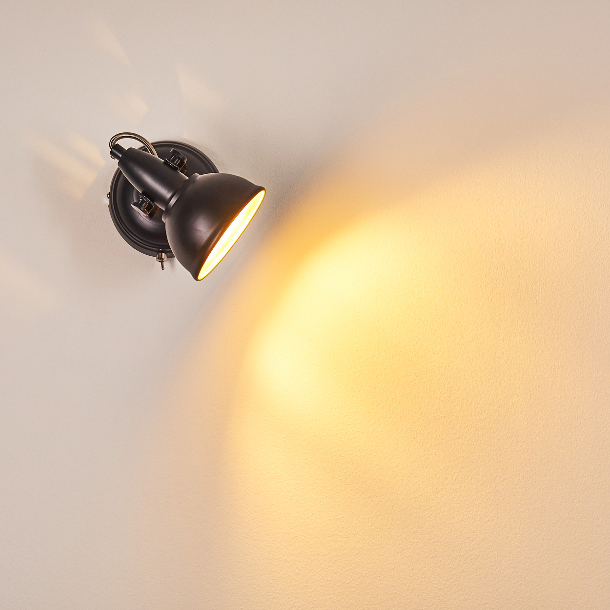 Eine schwarze Wandleuchte strahlt warmes Licht auf eine weiße Wand.