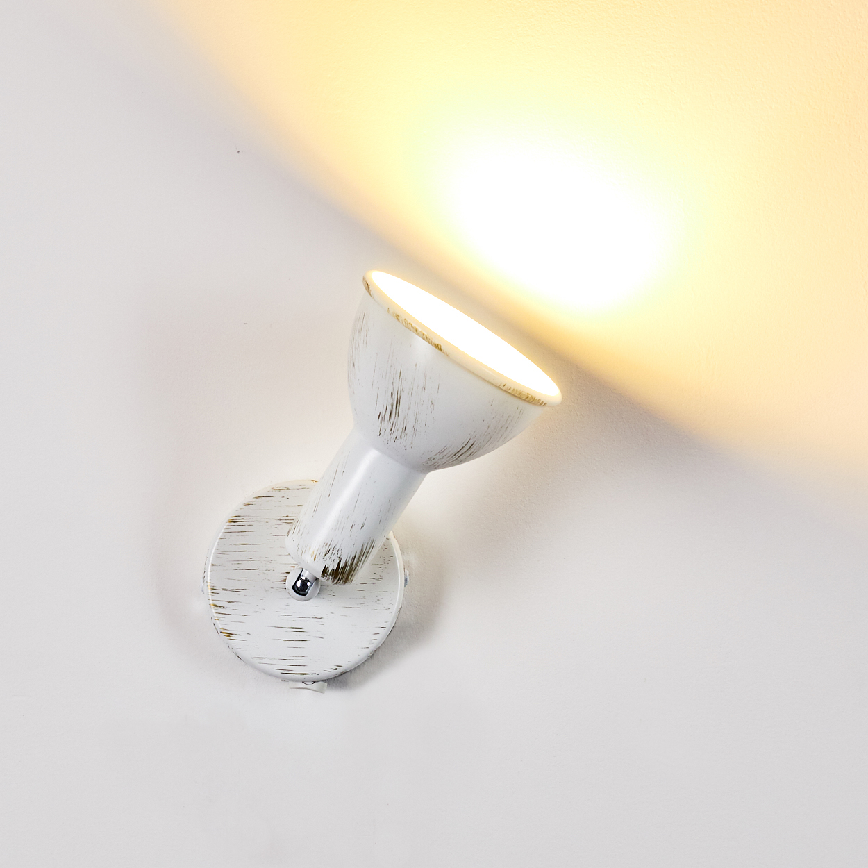Ein weißer Wandstrahler mit antikem Finish beleuchtet die Wand mit hellem Licht.
