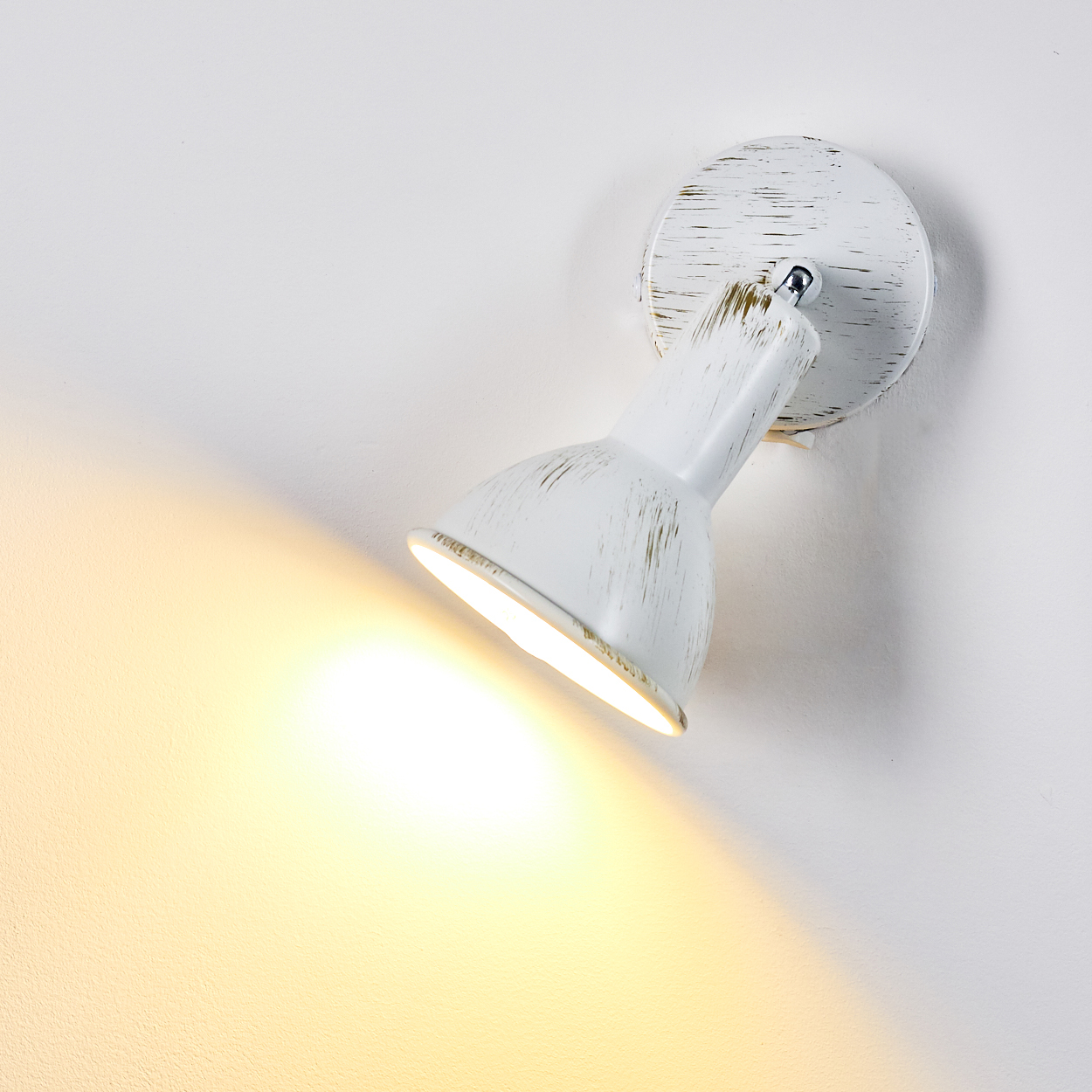 Eine weiße Wandleuchte mit verstellbarem Spot wirft helles Licht auf eine weiße Wand.