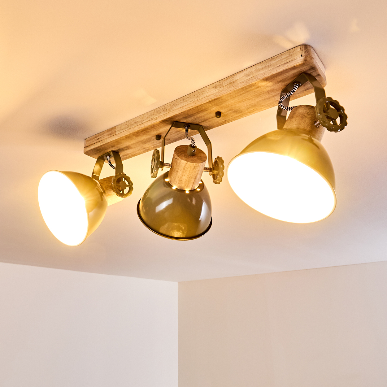 Eine Deckenleuchte mit drei gelben und grünen Lampenschirmen auf einem Holzbrett.
