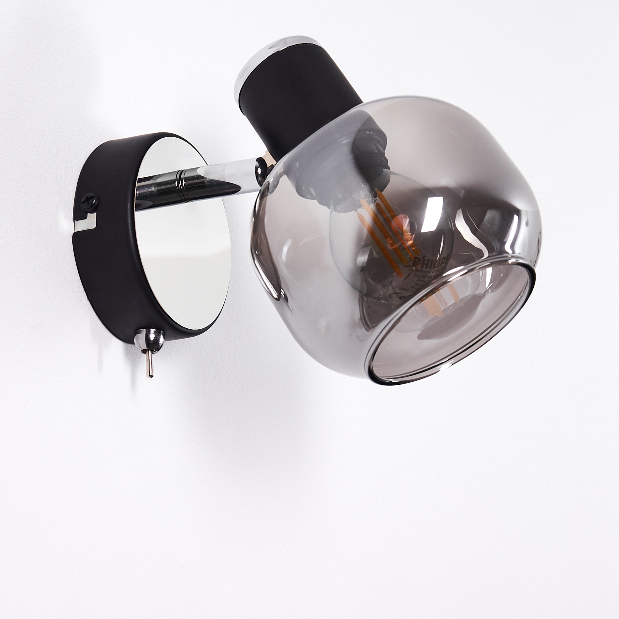 Eine moderne Wandleuchte mit schwarzem Sockel und rauchgrauem Glaslampenschirm.