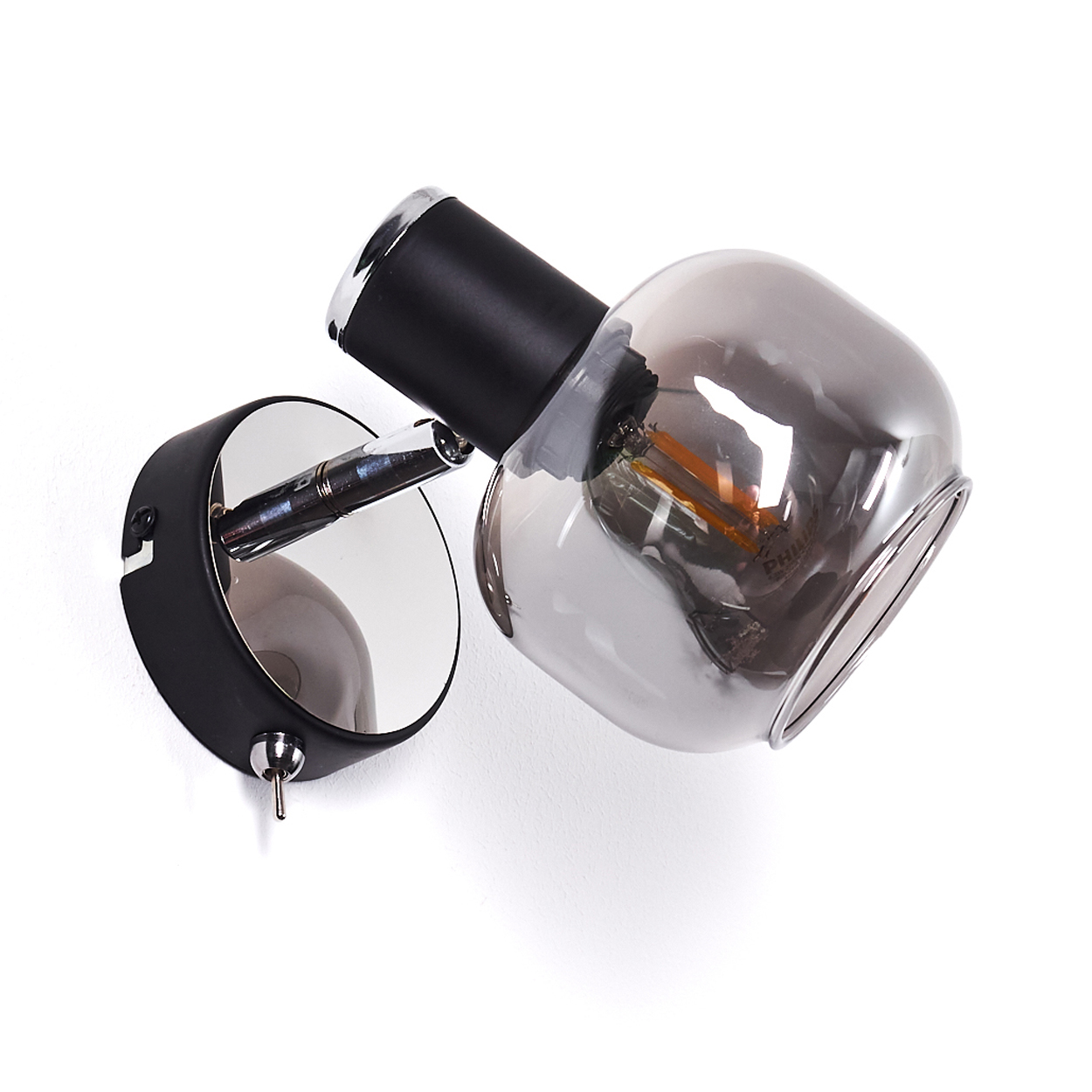 Eine moderne Wandlampe mit schwarzem Sockel, Chromarm und Rauchglas-Schirm.