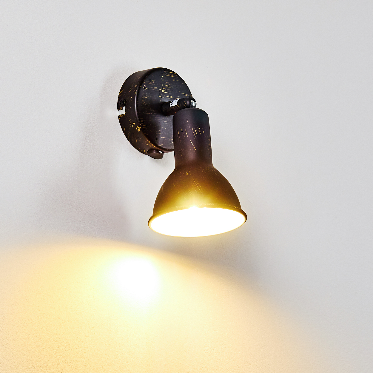 Eine dunkle Wandleuchte mit verstellbarem Spot wirft warmes Licht an eine weiße Wand.