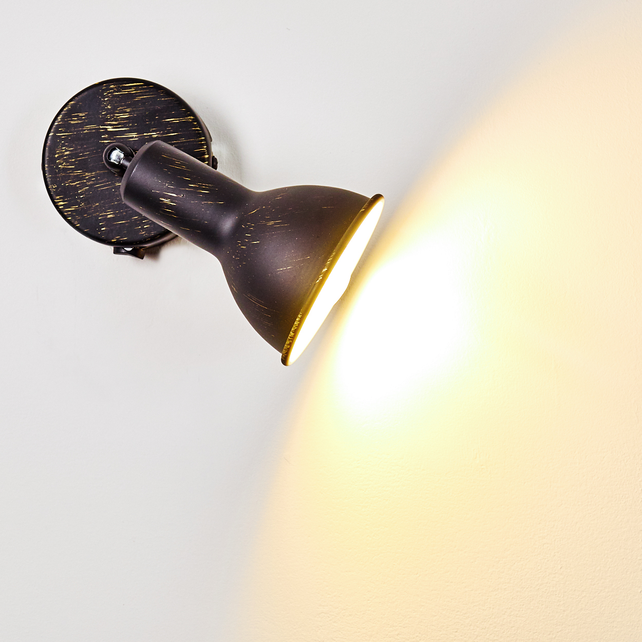 Ein dunkler Wandstrahler mit goldenen Sprenkeln beleuchtet eine weiße Wand.