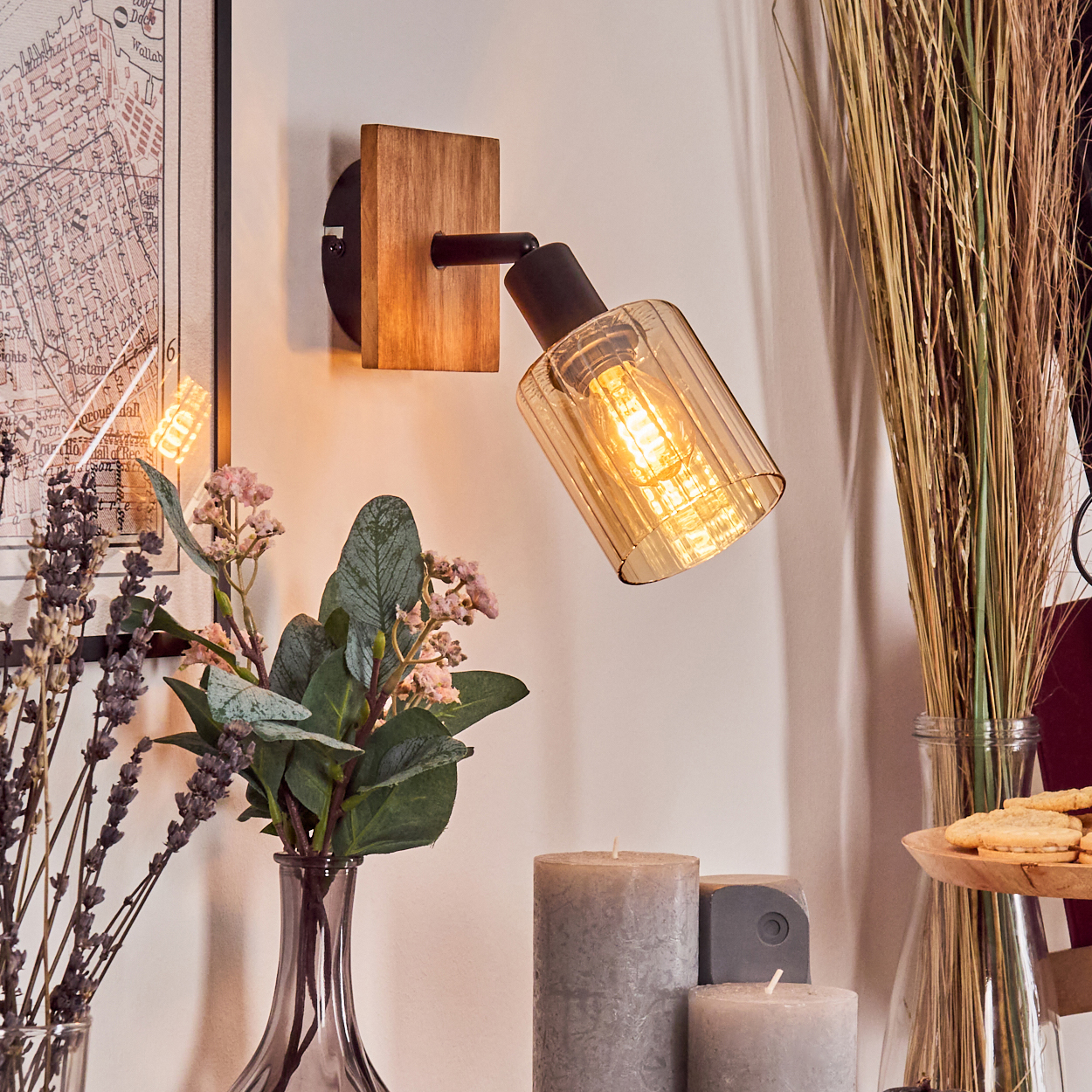 Ein Holzwandspot mit bernsteinfarbenem Glas leuchtet neben Vasen mit Pflanzen und Kerzen.