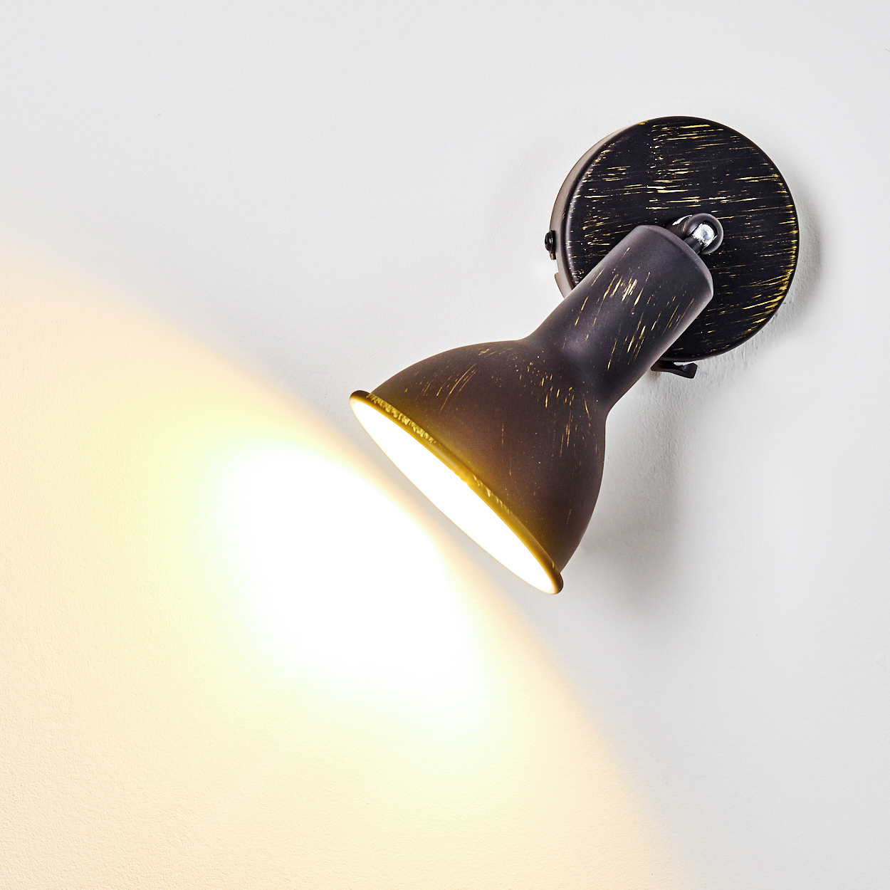 Eine schwarze Wandleuchte mit vergoldeten Akzenten leuchtet hell auf eine weiße Wand.