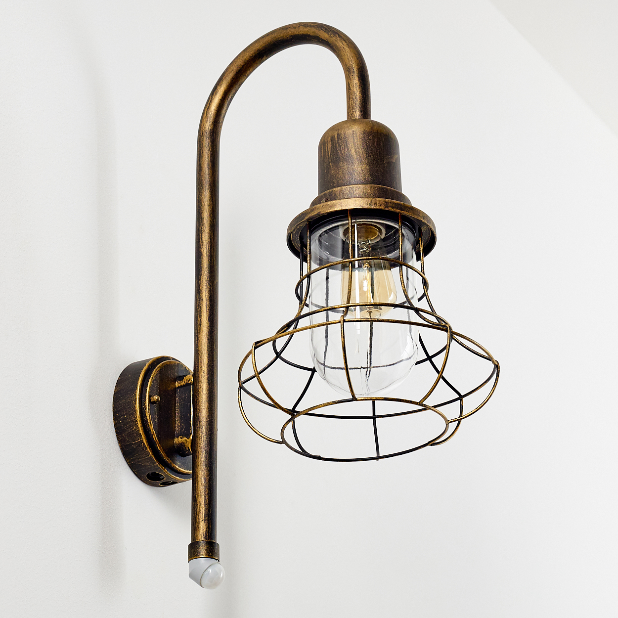 Eine bronzefarbene Wandleuchte im Industriestil mit einem Drahtkäfig und einer Glühbirne.