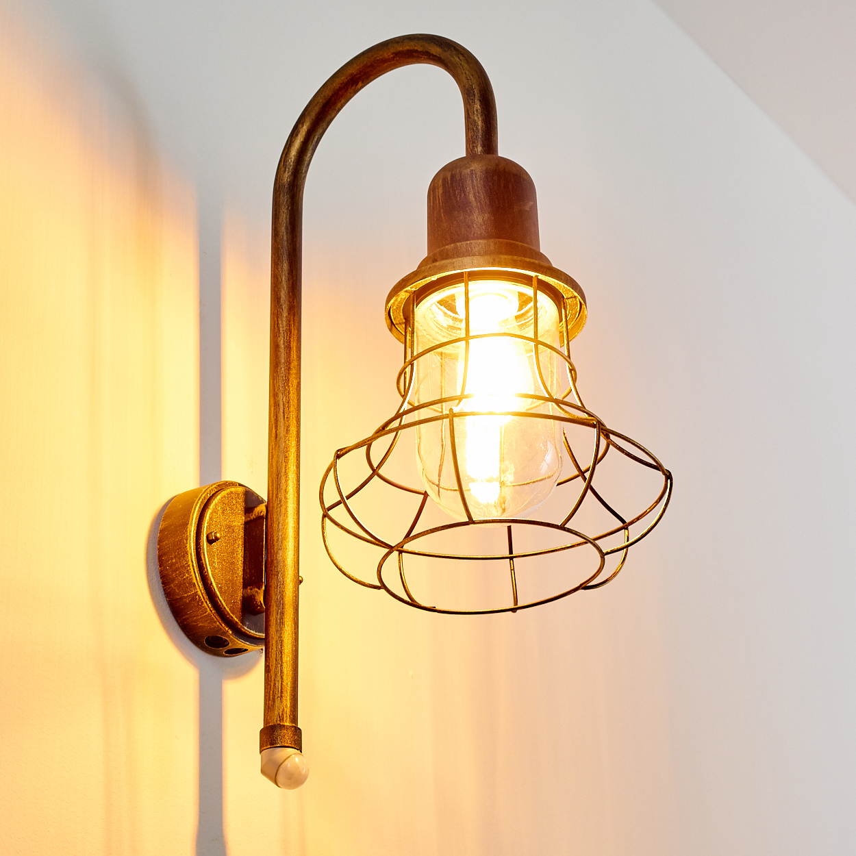 Eine Wandleuchte im Industrie-Stil mit einem Metallkäfig und sichtbarem Leuchtmittel.