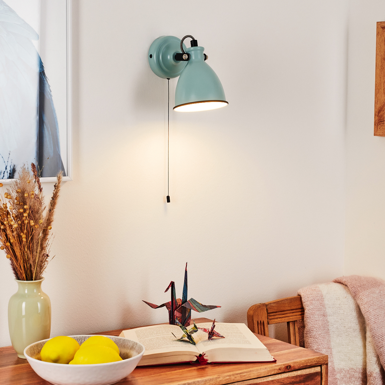 Ein Nachttisch mit einer Lampe, Buch, Papierkranichen, Zitronen und Deko-Zweigen.