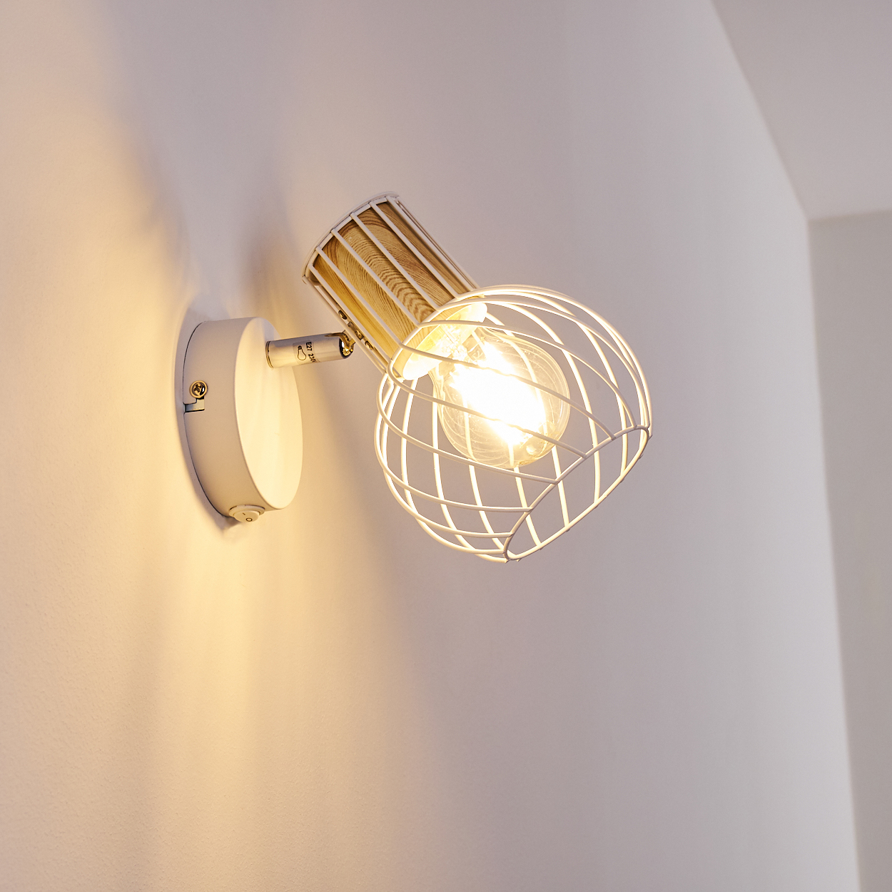 Eine weiße Wandleuchte mit Drahtkäfig und Holzdetail leuchtet.