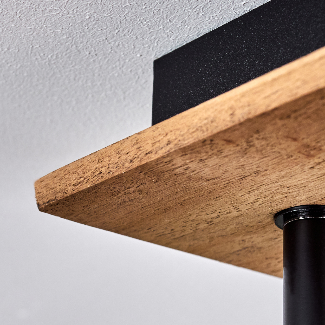 Nahaufnahme eines Holzregals mit schwarzer Metallstütze und strukturierter Decke.