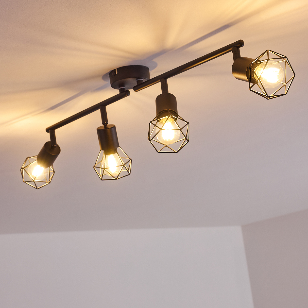 Schwarze Deckenleuchte mit vier Lampen und geometrischen Käfigschirmen.