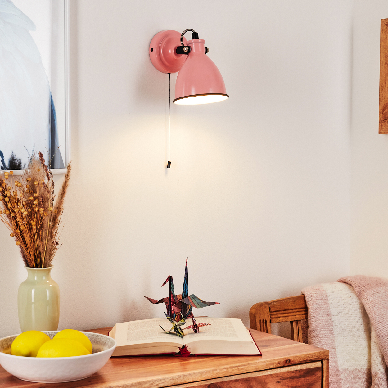 Eine rosa Wandlampe leuchtet über einem Buch mit Papierkranichen und Zitronen.